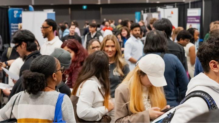 A busy exhibitor hall at the Halifax Universities Career Fair, with groups of students walking between employer booths and speaking with ...